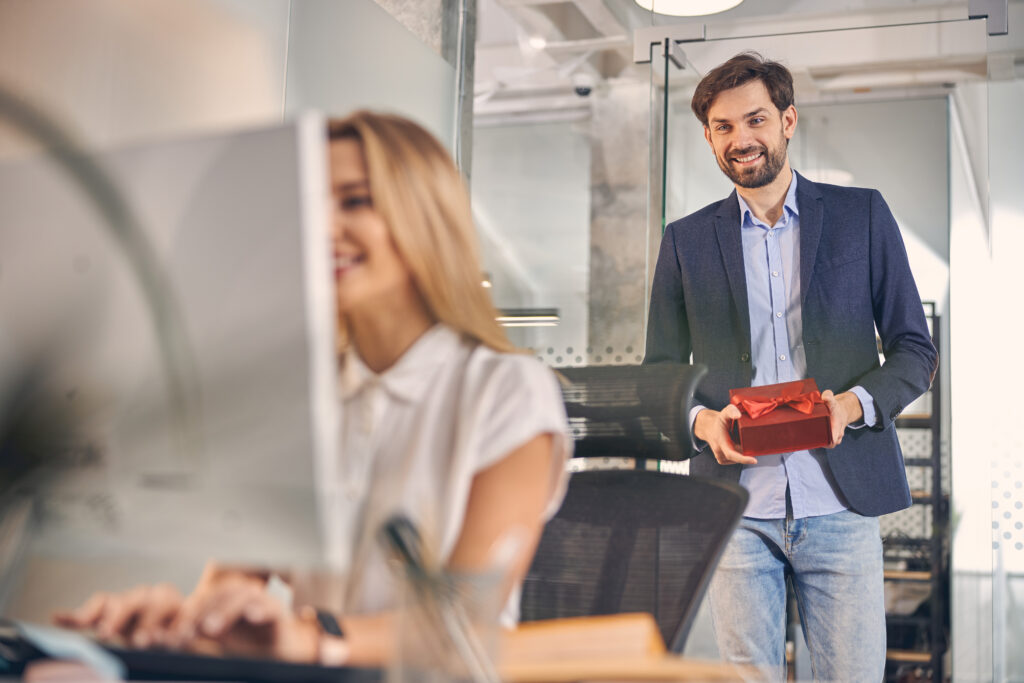 Admin professional working at desk with happy man walking up with gift