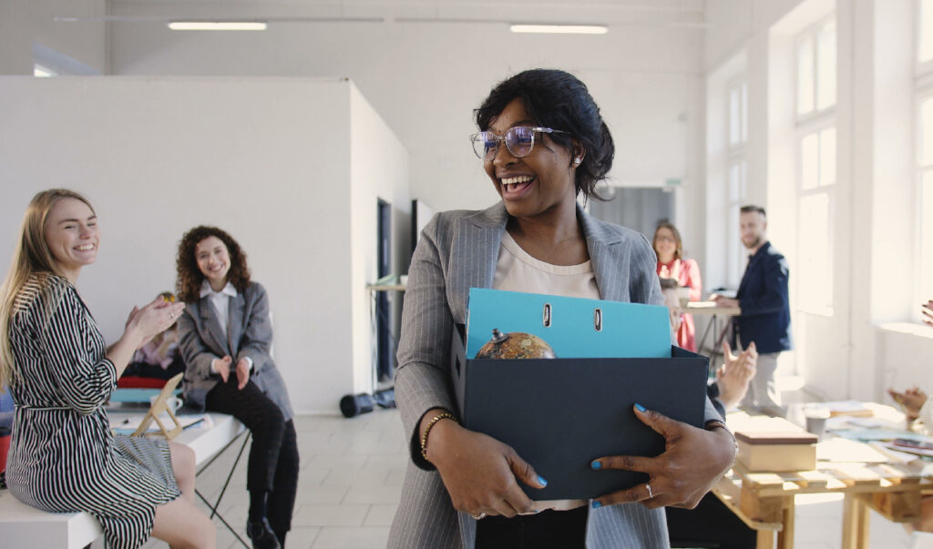 Woman walking into office on first day with employees saying, "welcome to the team"